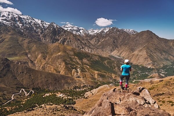 man standing on big rock looking at green valley