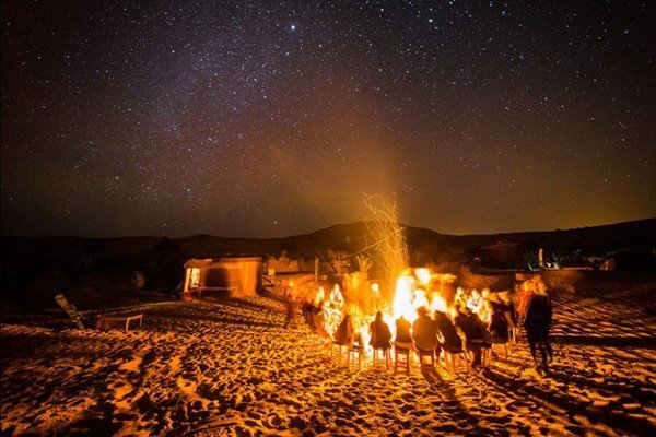 people siting around fire under the stars of desert