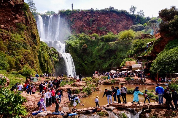 people crossing a bridge front of waterfalls